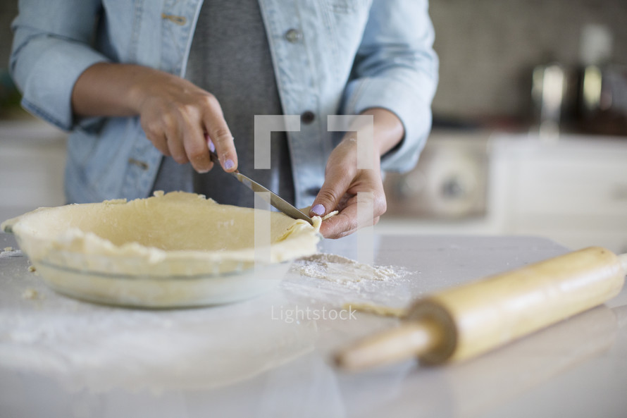A woman's hands trimming the edge of a pie crust.