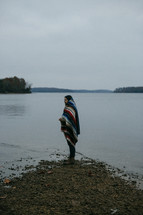a man wrapped in a blanket standing on a lake shore 