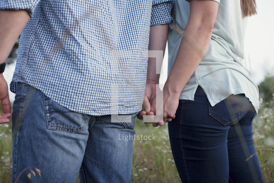 a couple holding hands standing in a field of tall grass 