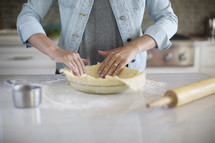 A woman placing a pie crust into a pie plate.
