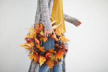 a woman holding a fall wreath 