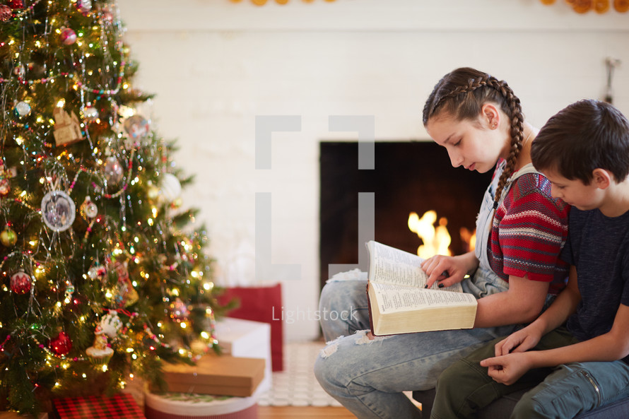 children reading a Bible around a Christmas tree
