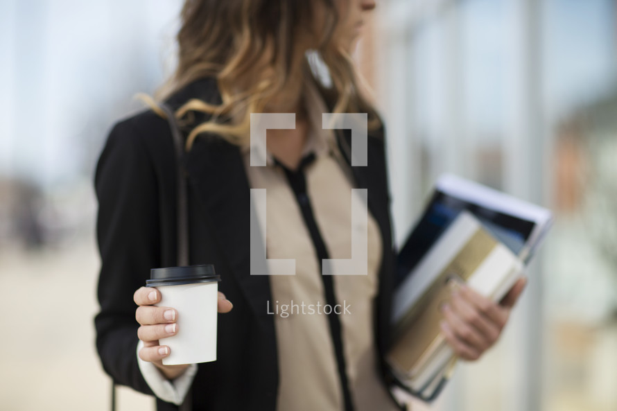 a career woman carrying a stack of books and a coffee cup 