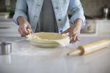 A woman placing a pie crust into a pie plate.