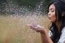 young woman blowing confetti in a field 