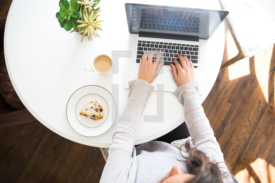 woman typing on a laptop computer with coffee and pastry on the table 