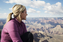 woman sitting at the edge of a canyon cliff looking out 