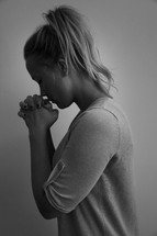 A young woman with her hands clasped together in prayer.