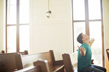 Man with arms extended while praying in a church pew.