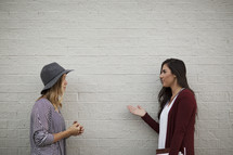friends standing in front of a white wall with one holding a Bible and journal talking, inviting a friend to join a Bible study 