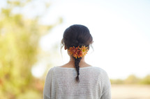 a woman with a braid and flowers in her hair standing outdoors 