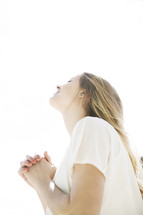 a woman with praying hands in intense sunlight looking up to God 