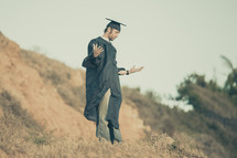 graduate standing outdoors with his arms outstretched in prayer