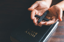 Wooden cross in open hands on a Bible