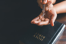 Hands holding a silver cross on a Bible