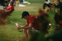 man holding a water bottle sitting in a chair at an outdoor concert 