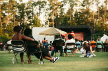 people sitting in folding chairs at an outdoor worship service 