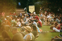 people sitting in the grass at an outdoor concert 