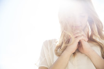 a woman with praying hands standing in intense sunlight 