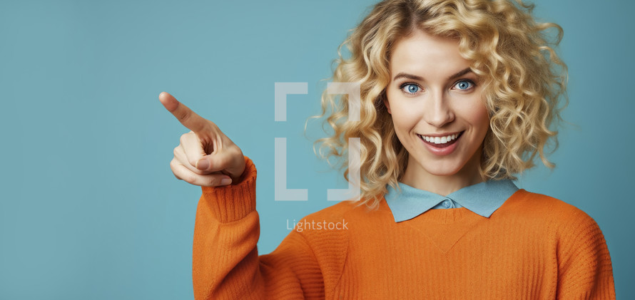 Joyful young woman with blonde curly hair, pointing finger, wearing an orange sweater and blue collar, with a vibrant teal background.