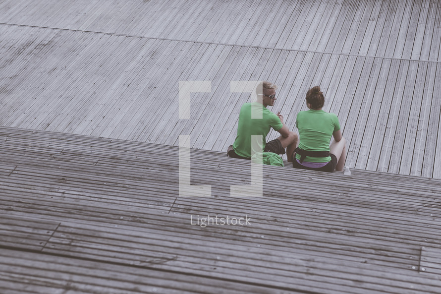 a couple sitting outdoors on a boardwalk talking 
