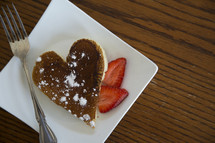 heart shaped pancake on a plate with strawberries.
