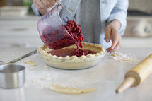 Hands pouring cherries into a prepared pie crust.