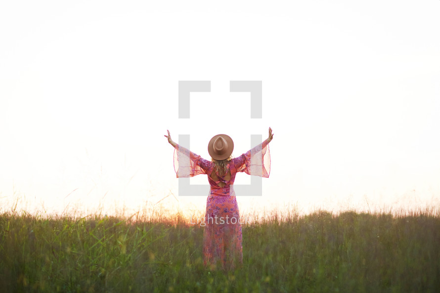 a woman in a pink dress walking through a field with arms raised
