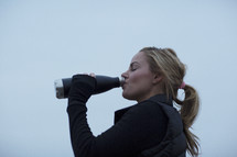 A woman drinking water from a stainless steel water bottle.