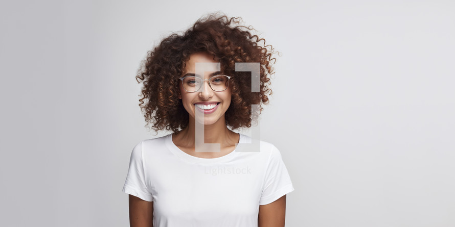 Smiling young woman with curly hair and stylish glasses on a light background.
