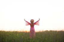 a woman in a pink dress walking through a field with arms raised