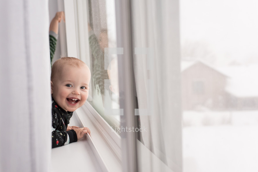 toddler boy looking out a window at snow 