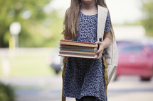 a young girl holding books walking to school 