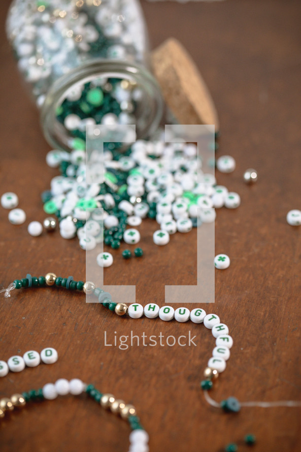 Jar of green, white, and gold beads with word - thoughtful
