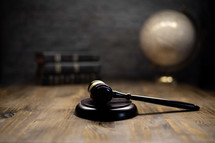 a gavel on a wooden table with bibles and globe in the background 