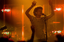 woman singing into a microphone with raised hands 