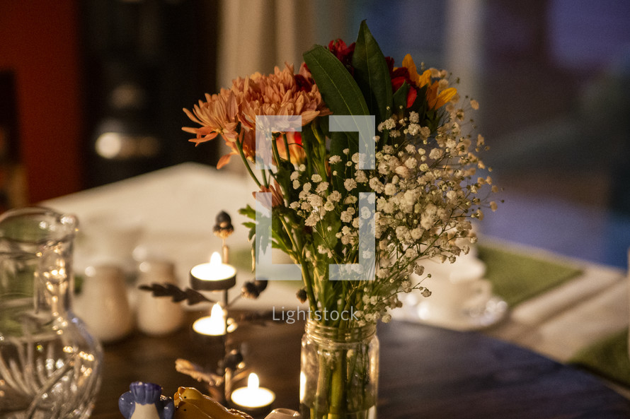 Small bouquet of flowers in a jar on table with candles