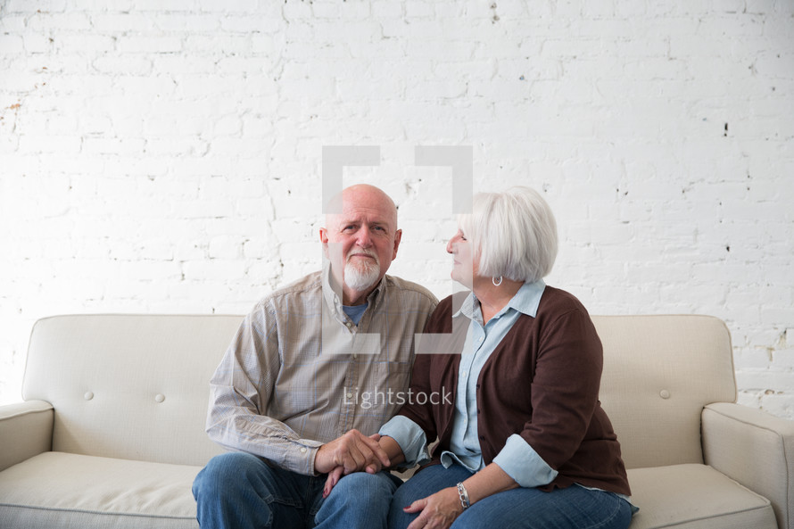 an elderly couple sitting on couch holding hands 