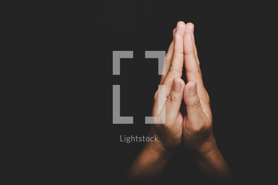Hands pressed together in prayer on a black background