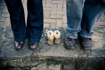 expectant parents standing beside empty baby shoes