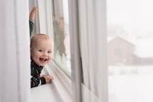 toddler boy looking out a window at snow 