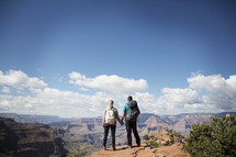 man and woman standing at the edge of a canyon cliff holding hands 