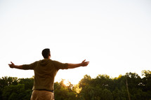 a man standing outdoors at sunset with outstretched arms 
