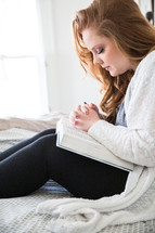 young woman sitting in bed reading and praying 