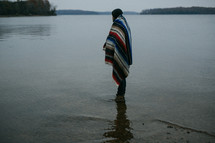 man wrapped in a blanket standing in water 