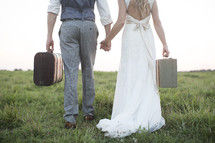 bride and groom carrying luggage in an open field. 