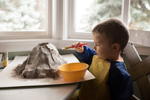 boy painting a paper mâché volcano project 