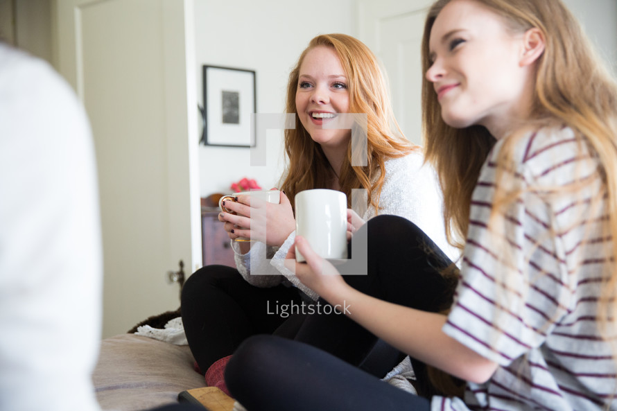 young women sitting on a bed drinking coffee and talking 