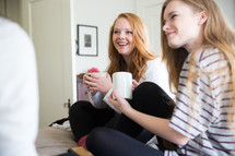 young women sitting on a bed drinking coffee and talking 