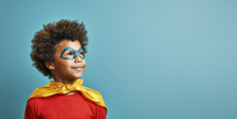 Inspired young boy in superhero costume with mask and cape, gazing upward with hope and imagination against a teal background.